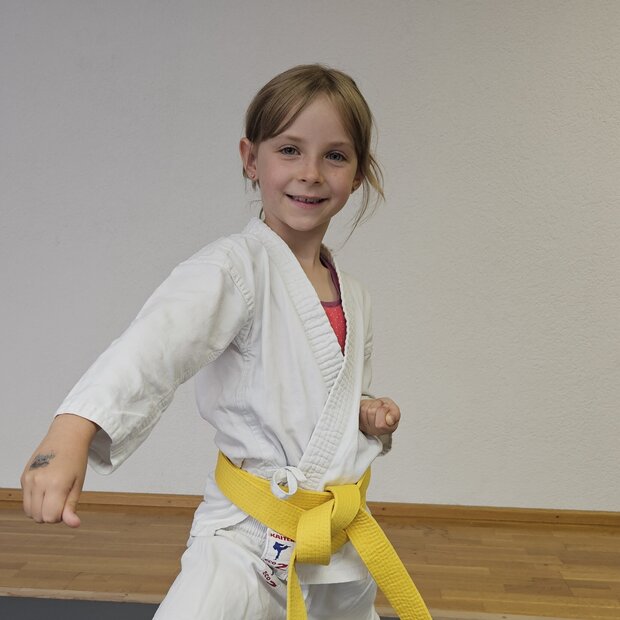Karate Kinder 5 bis 7 Jahre Ein lächelndes Mädchen im Karate-Anzug zeigt eine Abwehrbewegung